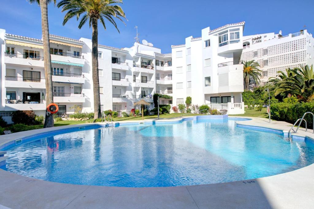 内尔哈Apartamento Las Palmeras的一座棕榈树的大型游泳池位于酒店大楼前