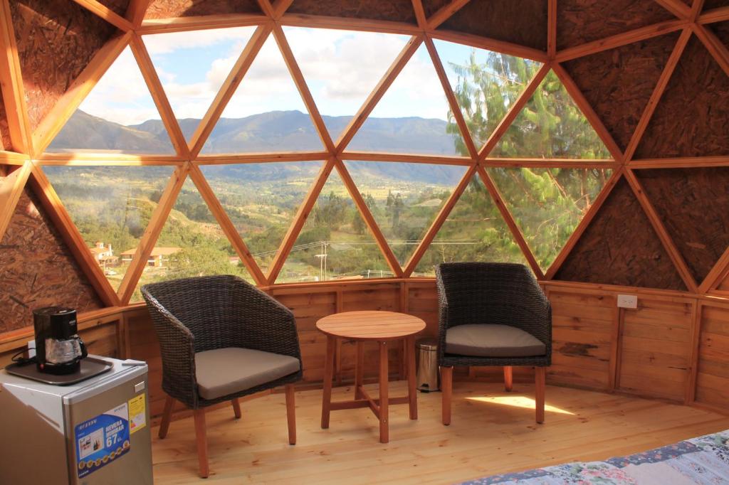 莱瓦镇Glamping y Chalet Aventura Park Villa De Leyva La Periquera的配有大窗户的客房内配有两把椅子和一张桌子