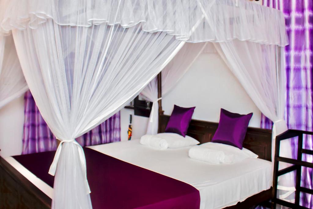 坦加拉Star Light Cabanas & Restaurant的一间卧室配有一张带紫色窗帘的天蓬床