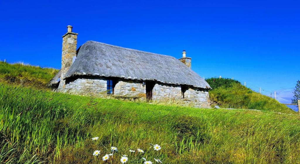 ElgolTigh Lachie at Mary's Thatched Cottages, Elgol, Isle of Skye的一座古老的石头房子,茅草屋顶在山丘上