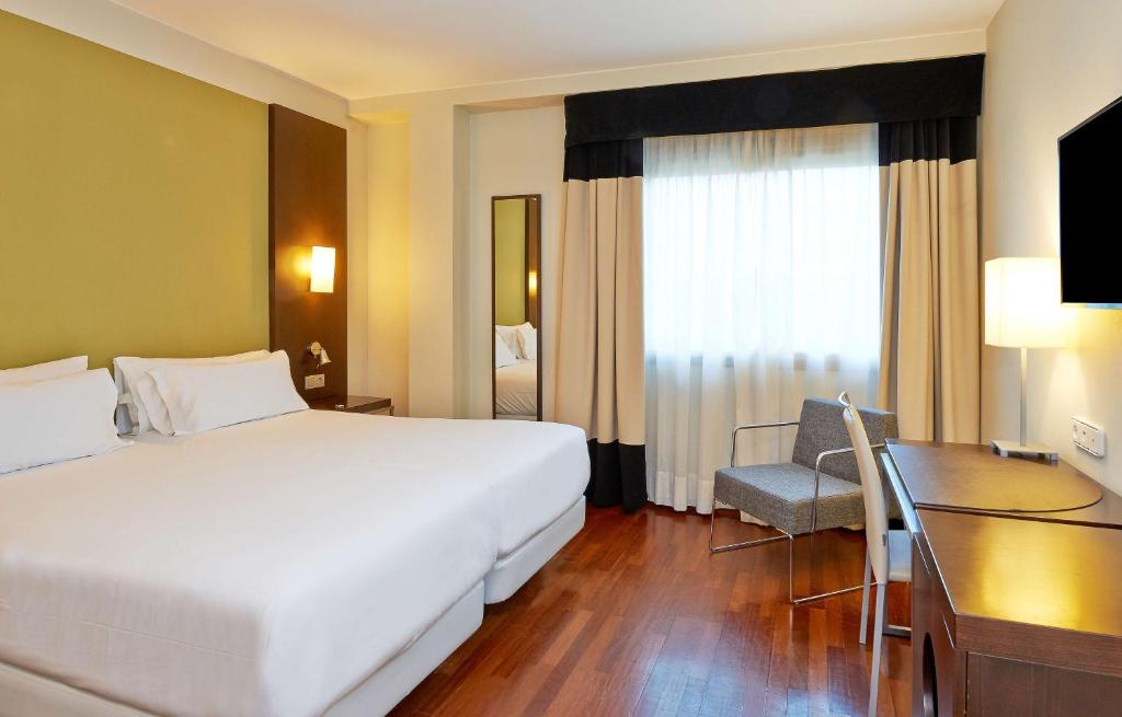 萨拉戈萨斯波特NH酒店的酒店客房设有一张大床和一张书桌。