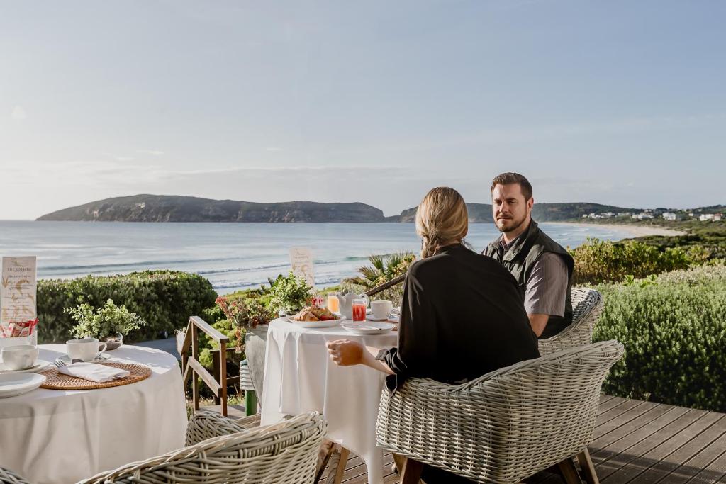 普利登堡湾The Robberg Beach Lodge - Lion Roars Hotels & Lodges的坐在桌子旁俯瞰大海的男人和女人