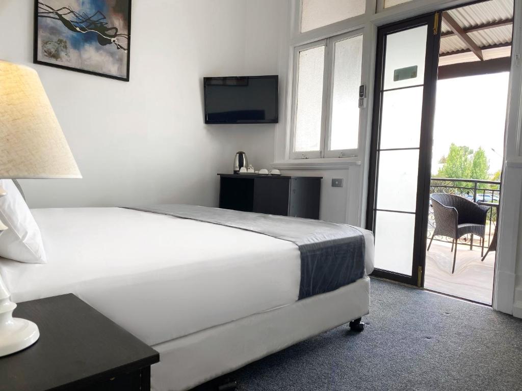 海伊Commercial Motel的一间卧室配有一张床、一台电视和一个阳台
