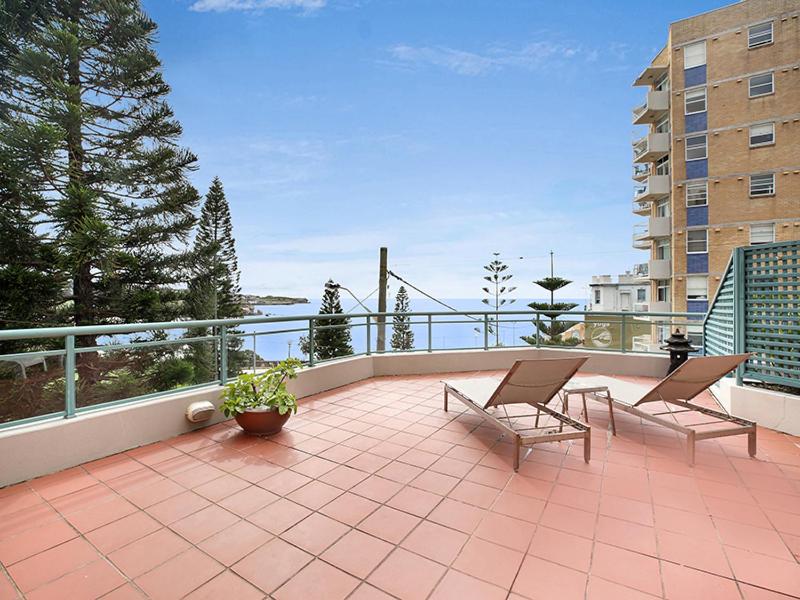 悉尼AeA库吉美景公寓酒店的阳台配有两把椅子和一张桌子,位于庭院