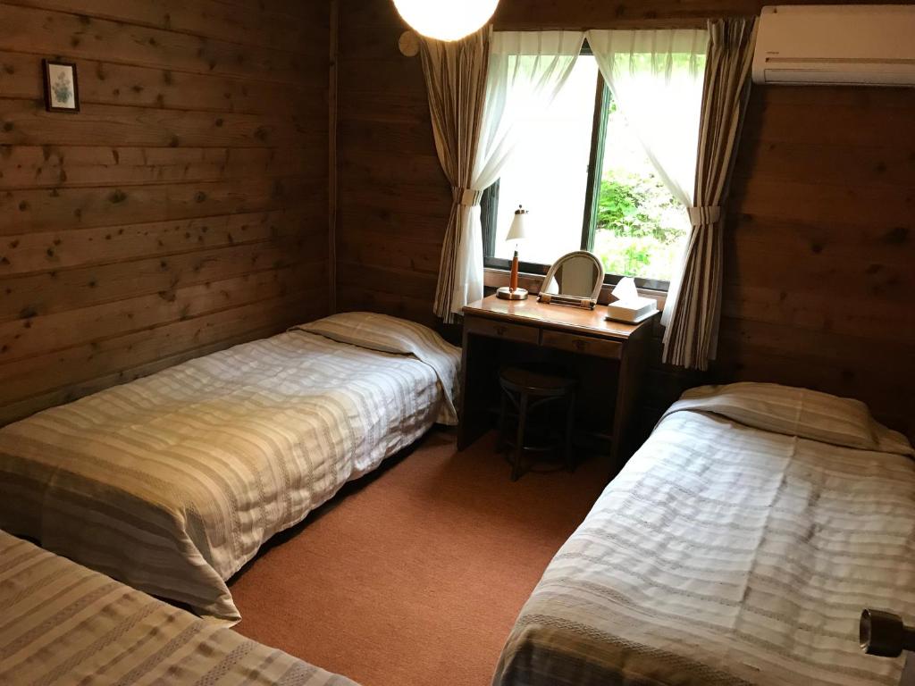 雫石町三轮车山林小屋的一间卧室设有两张床、一张桌子和一个窗口。