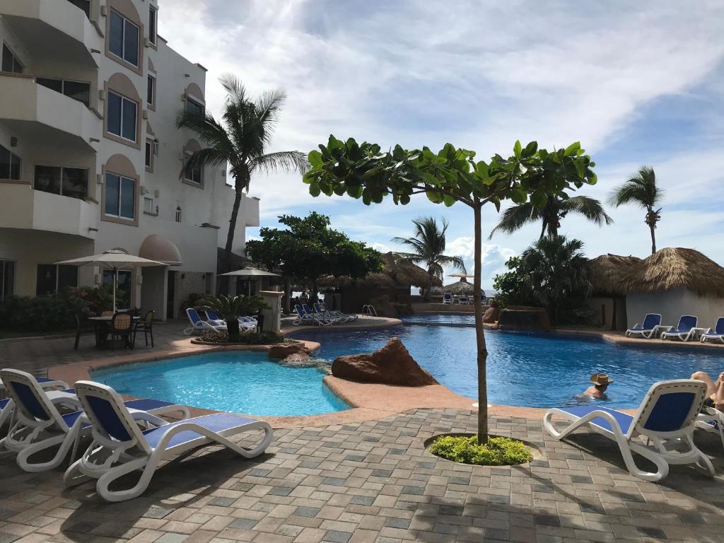 马萨特兰Costa Bonita Condominiums & Beach Resort - Primer planta的一座带椅子和棕榈树的酒店游泳池