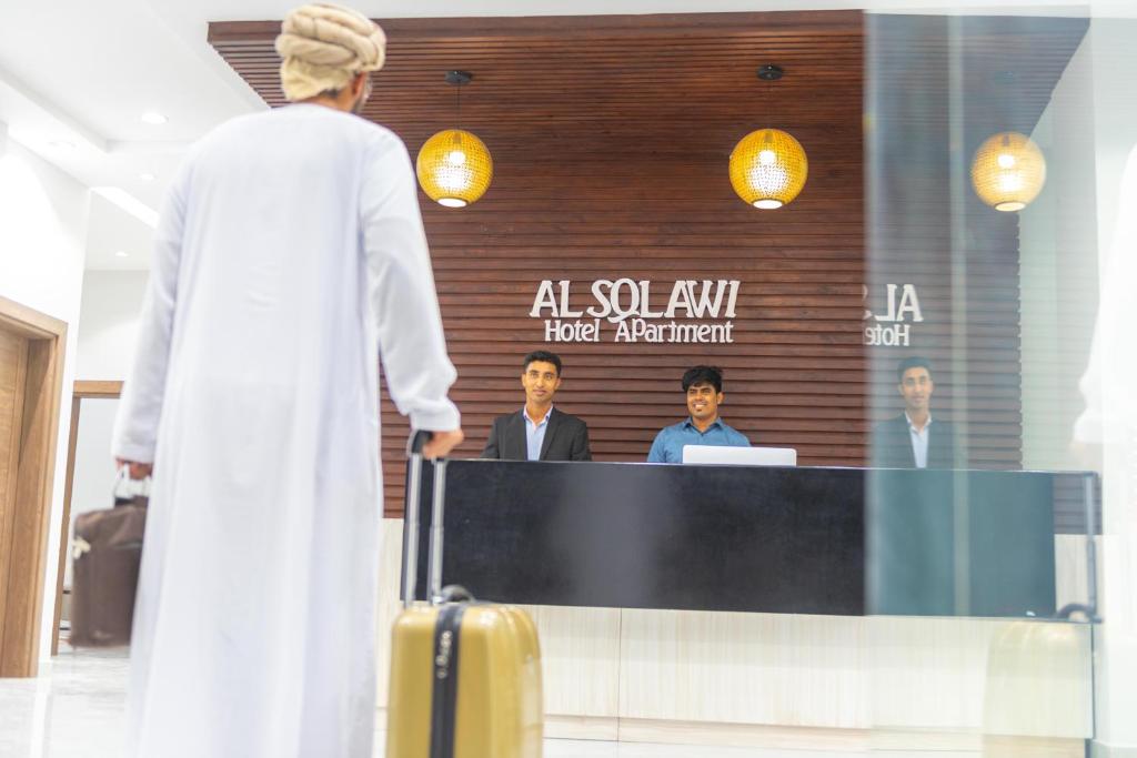 阿尔哈德Al Sqlawi Hotel Apartment的站在讲台前拿着手提箱的人