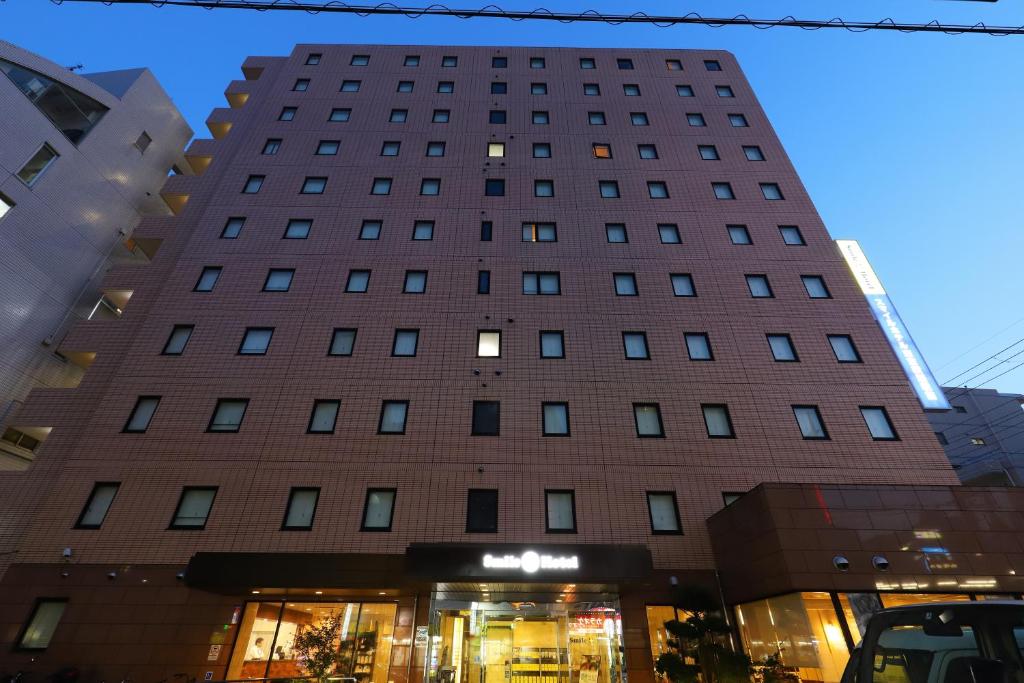 东京Smile Hotel Tokyo Ayase Ekimae的前面有一间商店的高楼