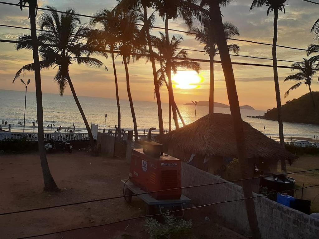 瓦斯科达伽马Leon Hide Out Guest House的棕榈树和海洋海滩上的日落