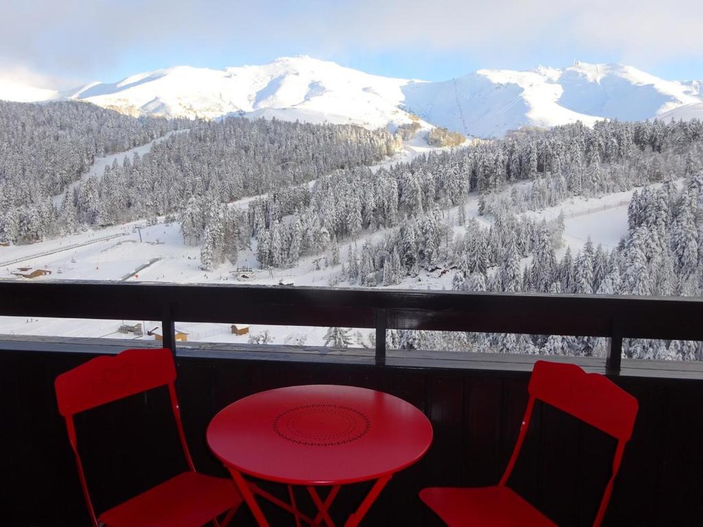 勒利然BIENVENUE AU LIORAN的雪覆盖的山景阳台上摆放着红色的桌椅