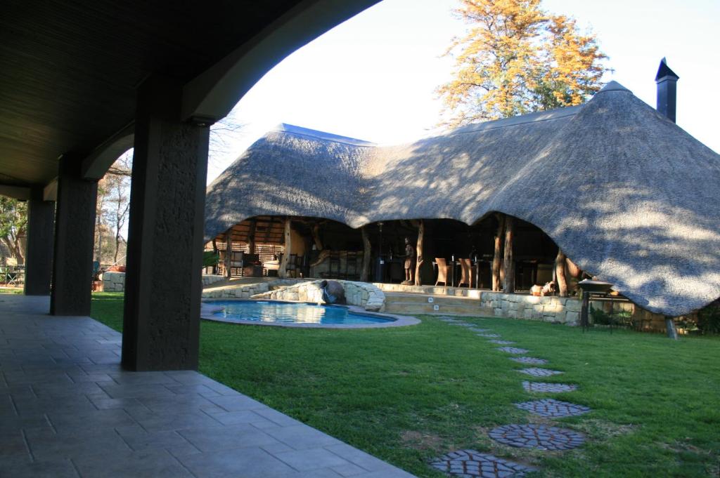 奥卡汉贾AFRICAN DREAMS GUESTHOUSE的一座带茅草屋顶的大型建筑,设有游泳池