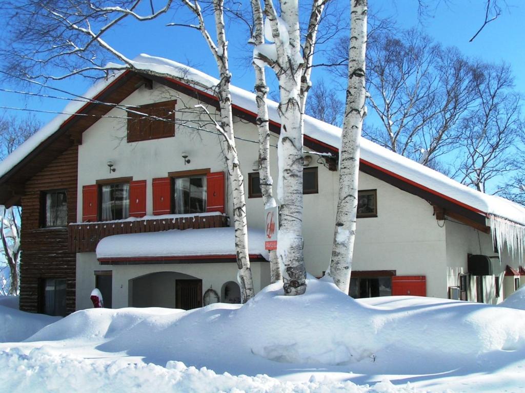 饭山市斑尾榆树膳食公寓的一座房子,前面有树木,被雪覆盖着
