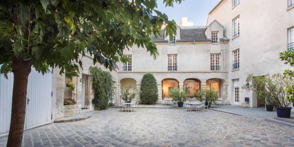 巴黎MIJE MARAIS Hostel的一座带桌子和树的建筑的庭院