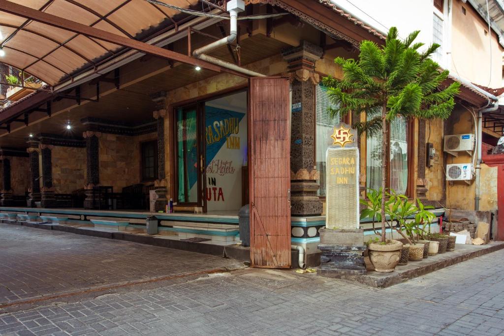 库塔Segara Sadhu Inn Kuta by ecommerceloka的前面有棕榈树的建筑