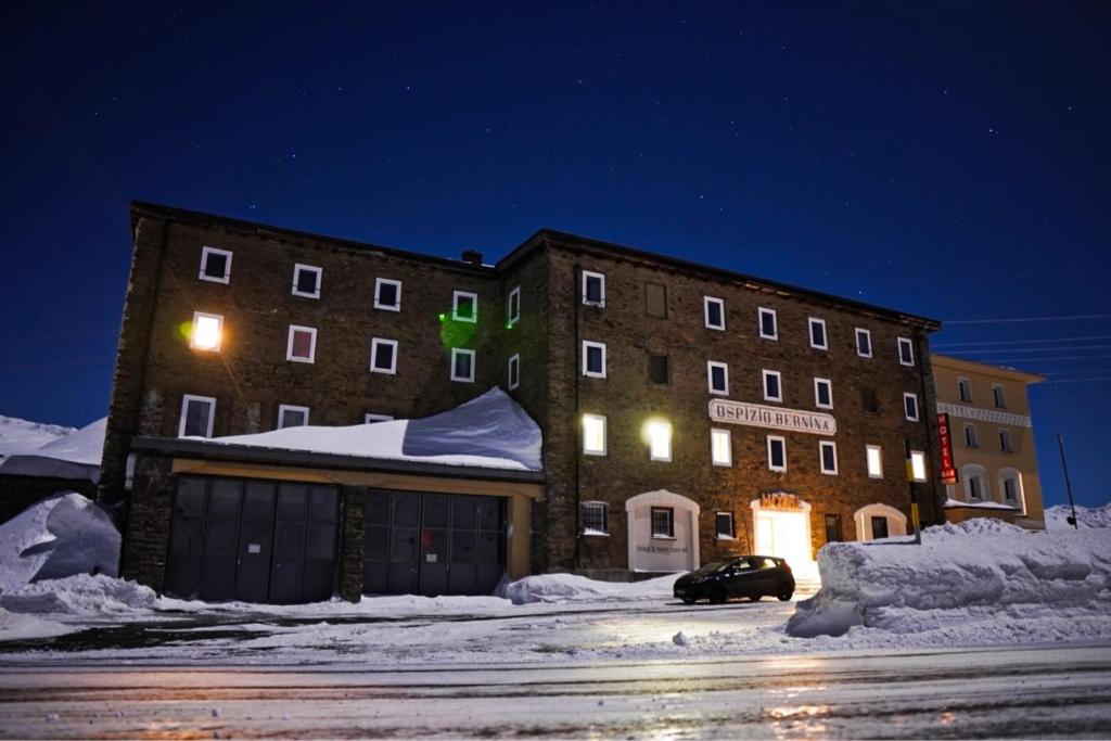 波尼纳豪瑟Hotel Bernina Hospiz的一座晚上在雪中停车的建筑物