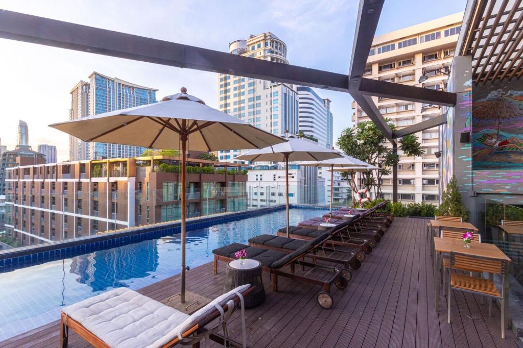 曼谷Hotel Icon Bangkok Sukhumvit 2的大楼内带桌子和遮阳伞的屋顶游泳池