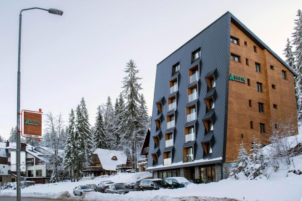 亚霍里纳Alpin Apartments Jahorina的雪中的一个建筑物,前面有汽车停放