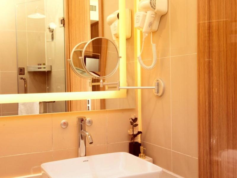 天津格林东方天津市武清区体育馆酒店的一间带水槽和镜子的浴室以及一部电话