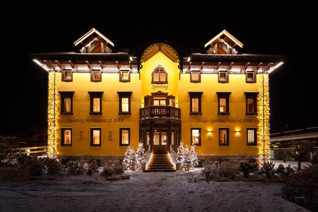 阿夏戈Asiago Sporting Hotel & Spa的一座黄色的大建筑,前面有圣诞灯