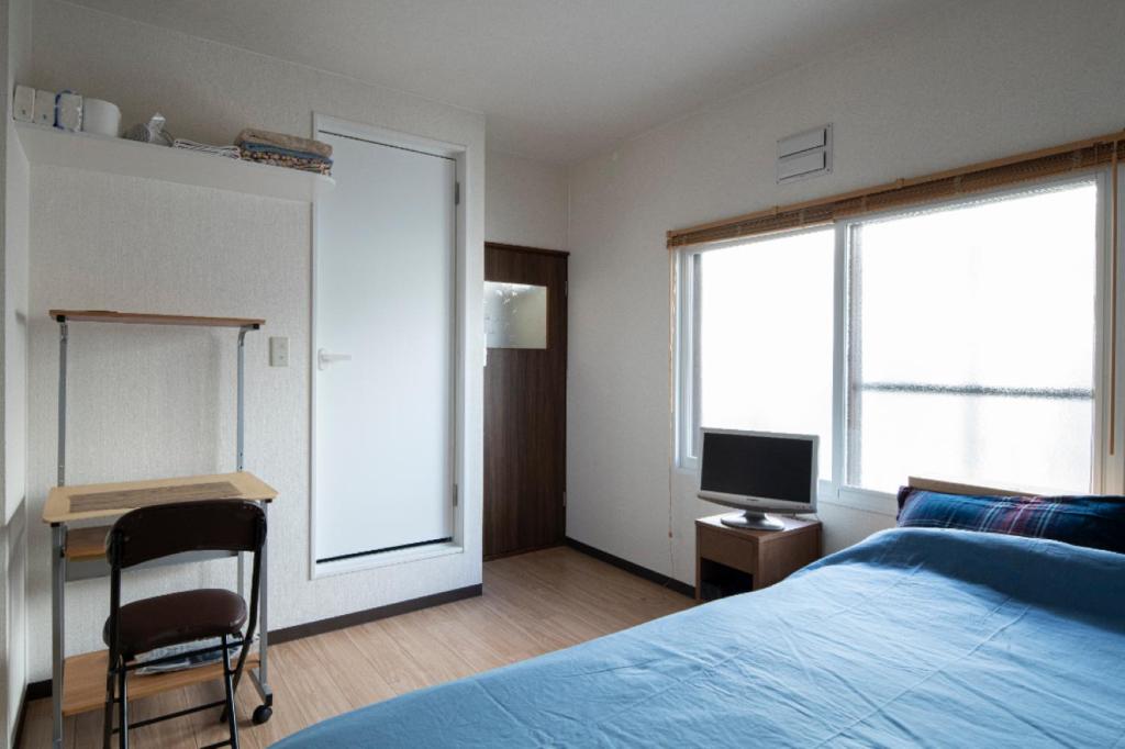 札幌Guesthouse Erimo Apartment的一间卧室配有一张床、一张书桌和一台电视