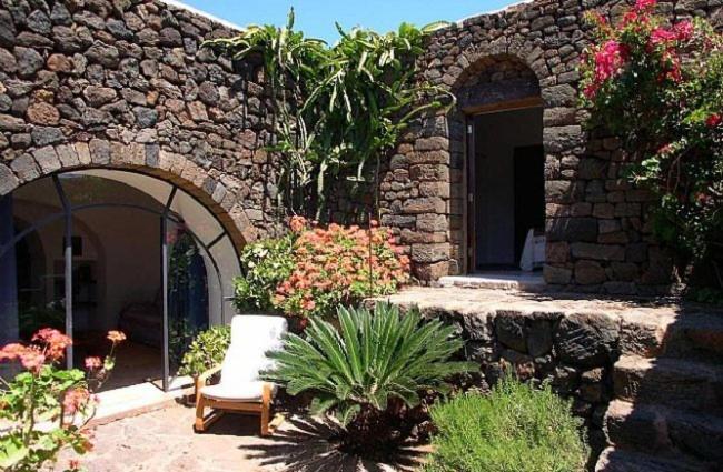潘泰莱里亚圣安娜达穆索度假屋的石头建筑,带椅子和一些花
