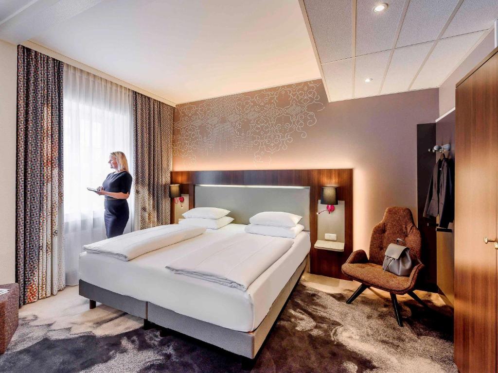慕尼黑慕尼黑奥林匹克公园美居酒店的一位妇女站在带大床的卧室