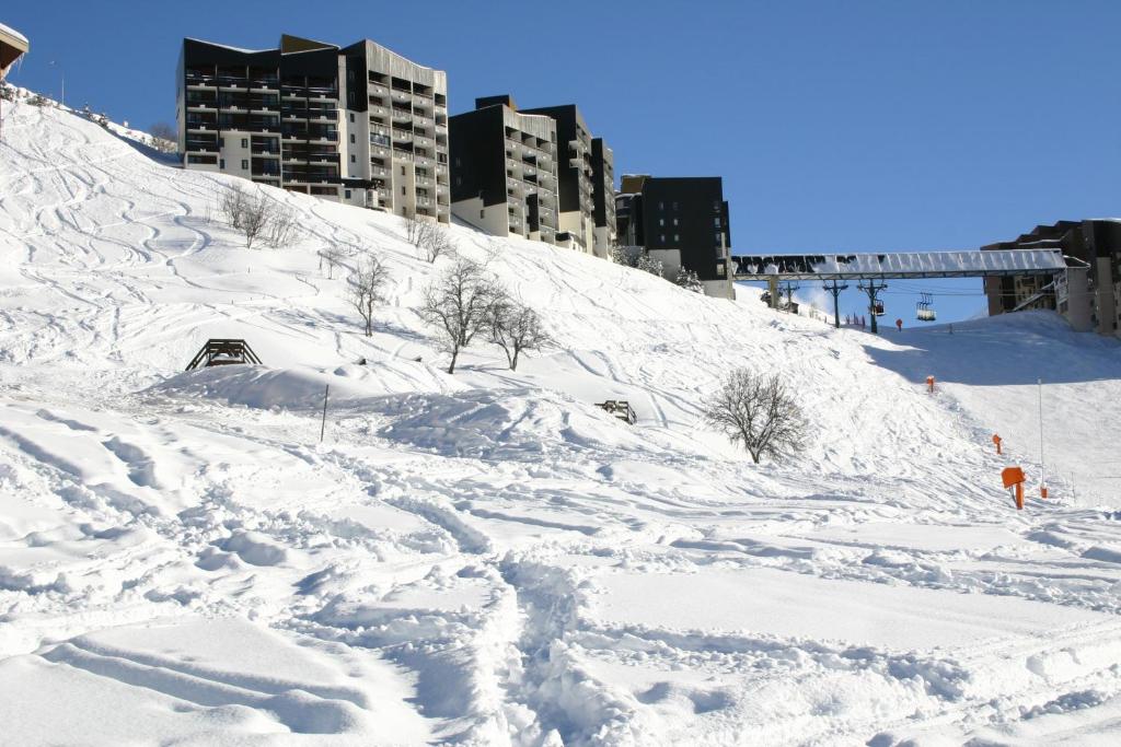 里蒙纽耶Azureva Les Menuires的一座有雪覆盖的山丘,其背景是建筑