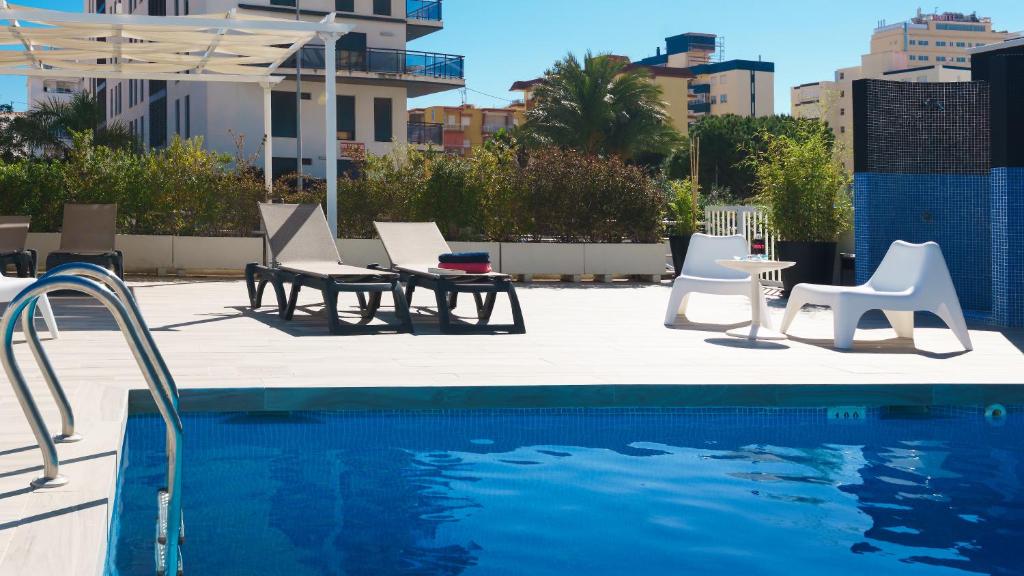 甘迪亚信天翁酒店的一个带白色椅子和桌椅的游泳池