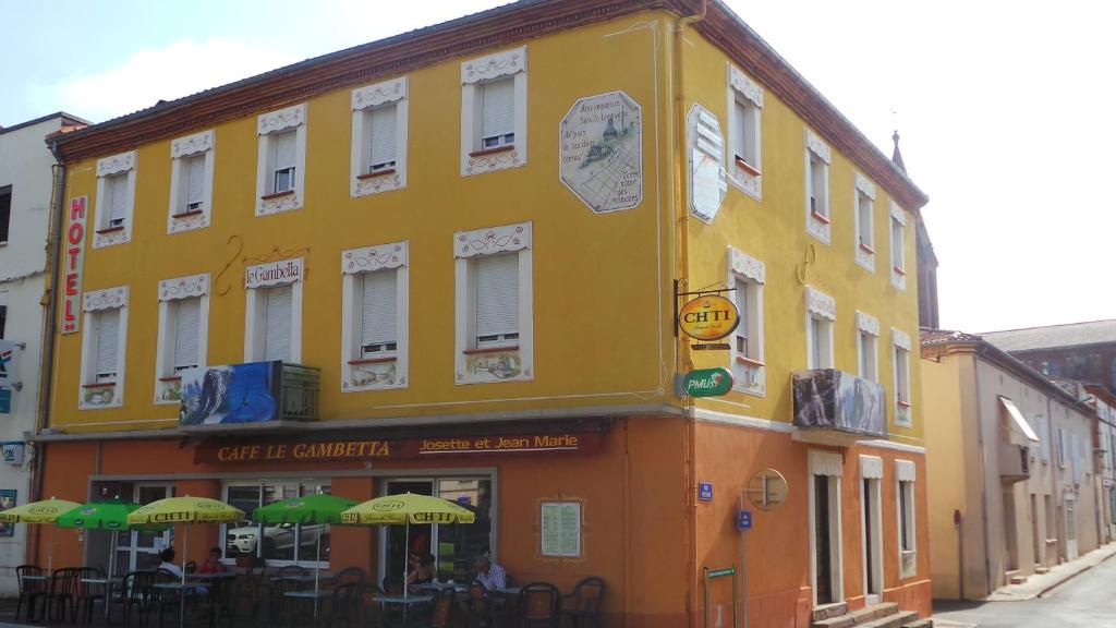 Carmaux勒甘贝塔酒店 的街上一座黄色的建筑,上面有桌子和遮阳伞