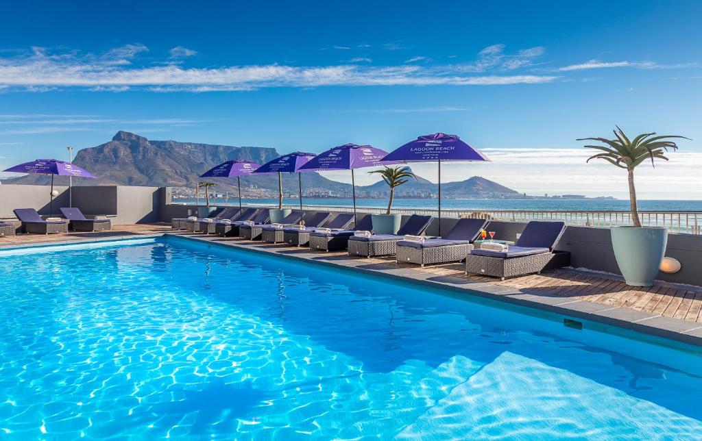 开普敦泻湖滩酒店及Spa的一座大楼内的游泳池,配有椅子和遮阳伞