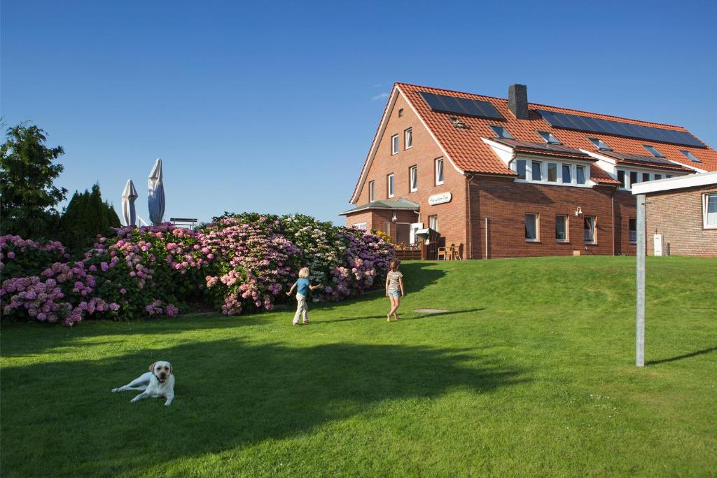 诺伊韦克岛Hotel Hus Achtern Diek的两个人和一只狗在房子前面的草地上