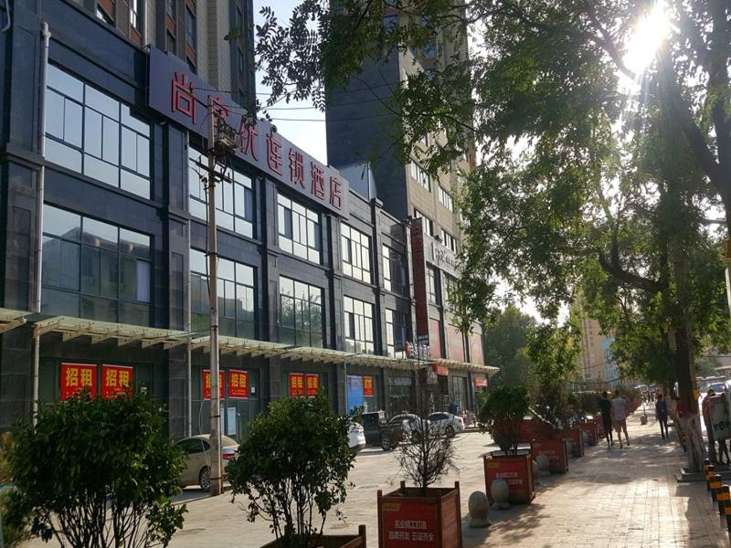 咸阳尚客优酒店陕西咸阳火车站店的城市街道上一座有树木和建筑的建筑