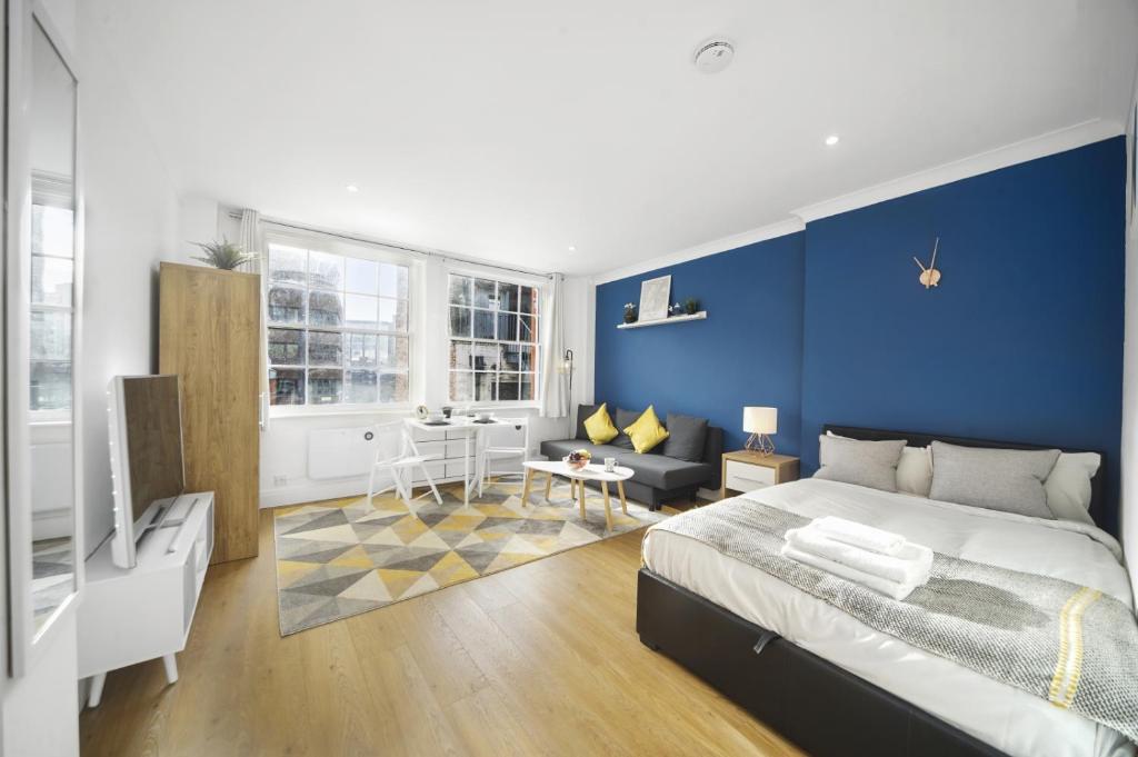 伦敦Studio Apartment by Homely Stays的卧室拥有蓝色的墙壁,配有一张床和一张沙发