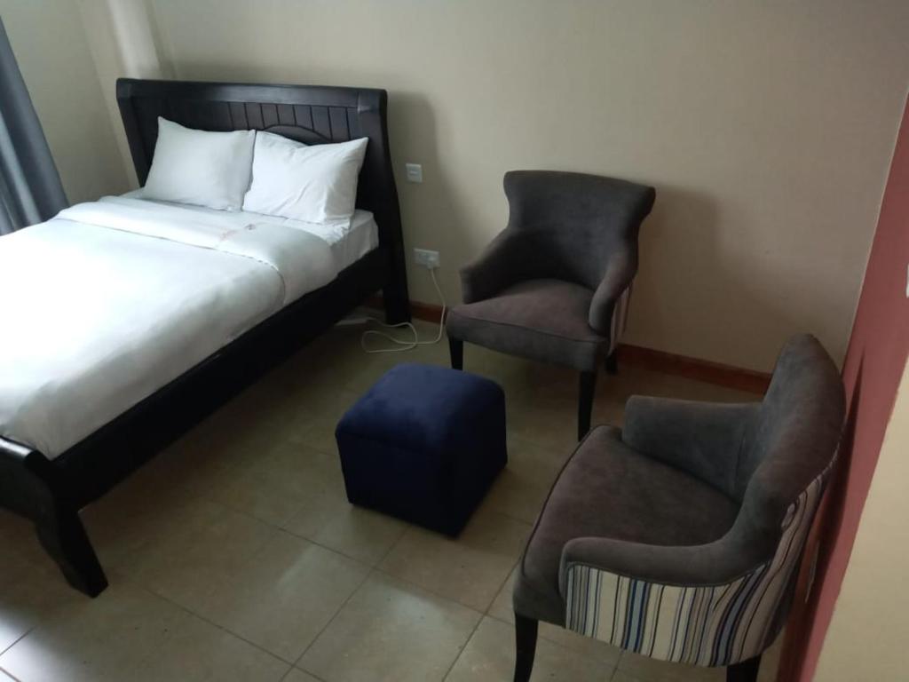 内罗毕Nairobi west suite的一间卧室配有一张床、两把椅子和一张搁脚凳