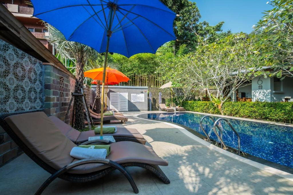 卡伦海滩Kata Tranquil Villa - SHA Plus的一组椅子和一把遮阳伞,位于游泳池旁