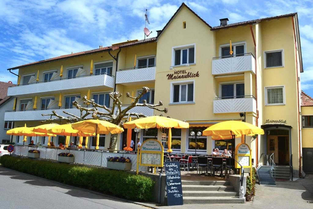 乌尔丁根-米赫尔霍芬Hotel & Restaurant Mainaublick的前面设有桌子和遮阳伞的酒店