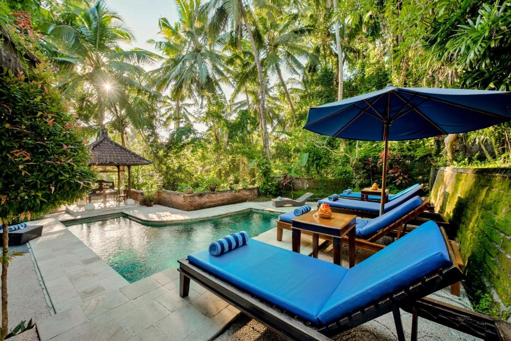 乌布Kebun Indah Ubud的一个带2把蓝色躺椅和遮阳伞的游泳池