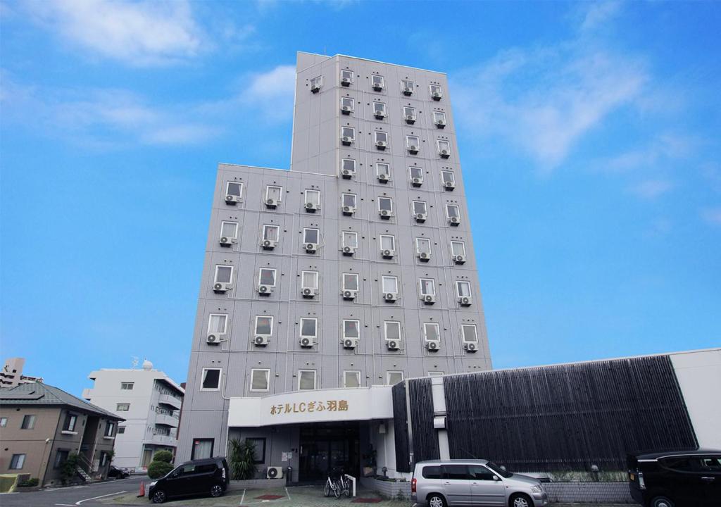 端岛Hotel LC Gifu Hashima的一座高大的白色建筑,前面有汽车停放