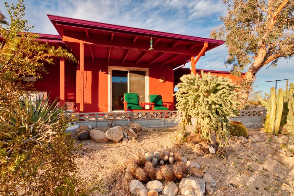 二十九棕榈村Chuck's Cabin in a Joshua Tree Community的前面有绿色椅子的红色房子