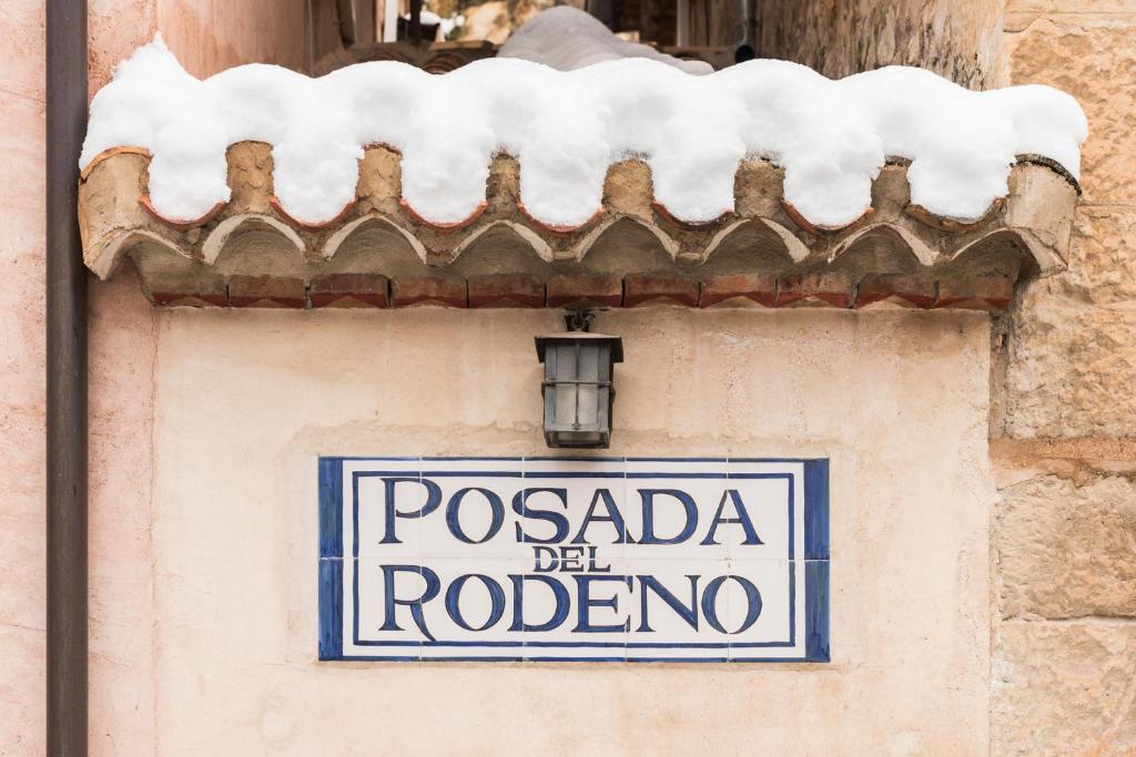 阿尔巴拉辛波萨达代尔罗德尼奥酒店的建筑物侧面的标志,有雪盖屋顶