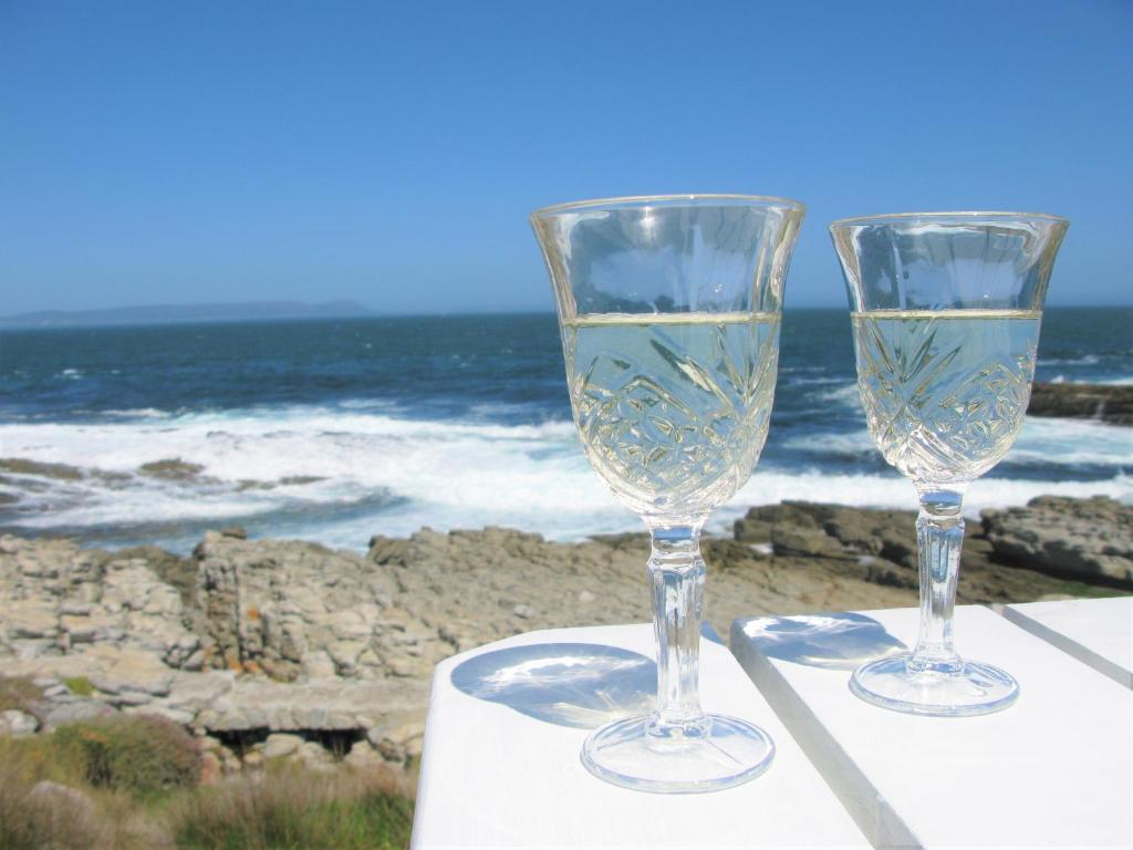 赫曼努斯Beachfront Cottage - Hermanus Whale View的两杯酒杯坐在靠近海洋的桌子上