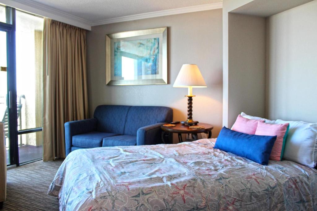 默特尔比奇Caravelle Resort by Palmetto Vacations的配有一张床和一把椅子的酒店客房