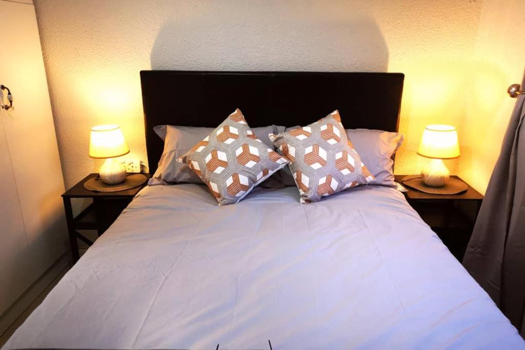 开普敦The Smiths Self Catering Cottage的一张带枕头的床和两张桌子上的两盏灯