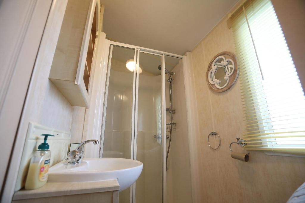 拉尔Lovely 4 berth static caravan, Marine Holiday Park, Rhyl, Wales的带淋浴和白色盥洗盆的浴室