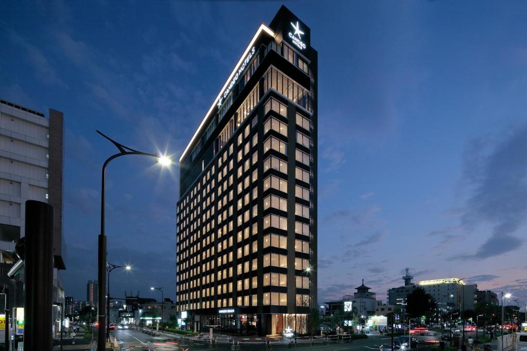 埼玉市大宫光芒酒店(Candeo Hotels Omiya)的一座高大的建筑,上面有钟