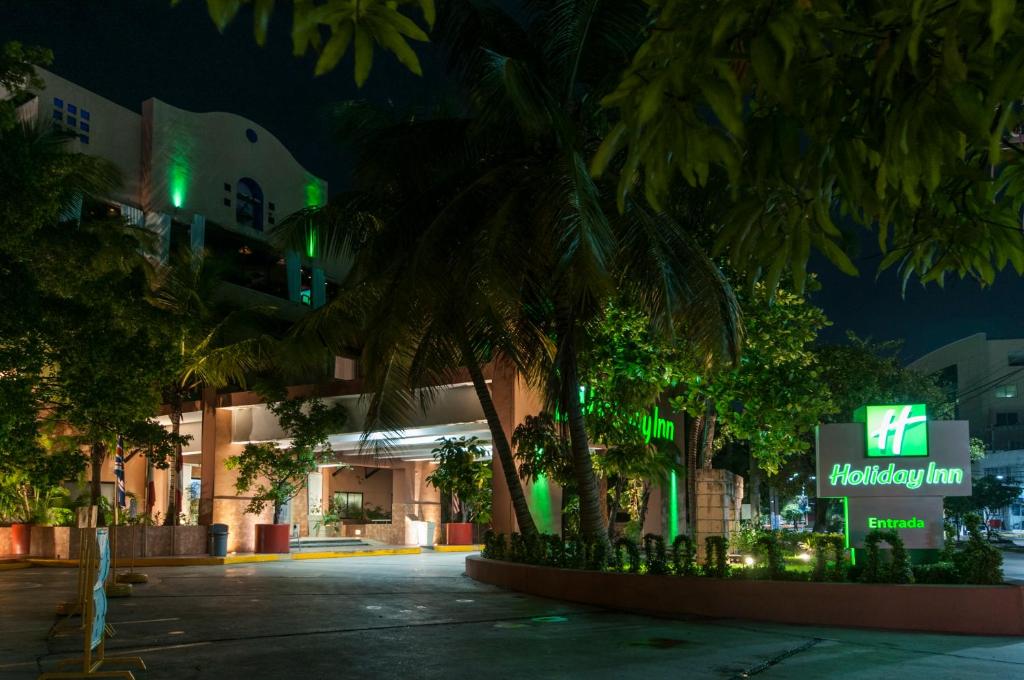 卡门城卡门城假日酒店的一座棕榈树在晚上的建筑