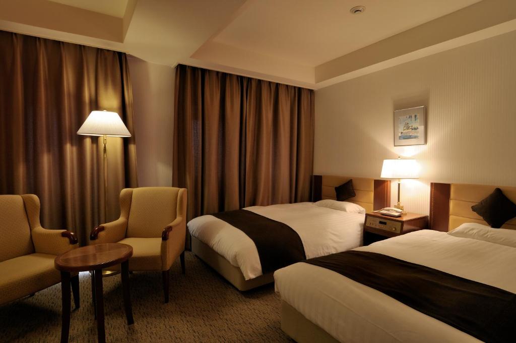 富山富山露台豪华酒店的酒店客房带两张床和一张桌子以及椅子。