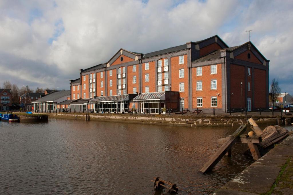 埃尔斯米尔港Holiday Inn Ellesmere Port/Cheshire Oaks, an IHG Hotel的水体旁边的一个大砖砌建筑
