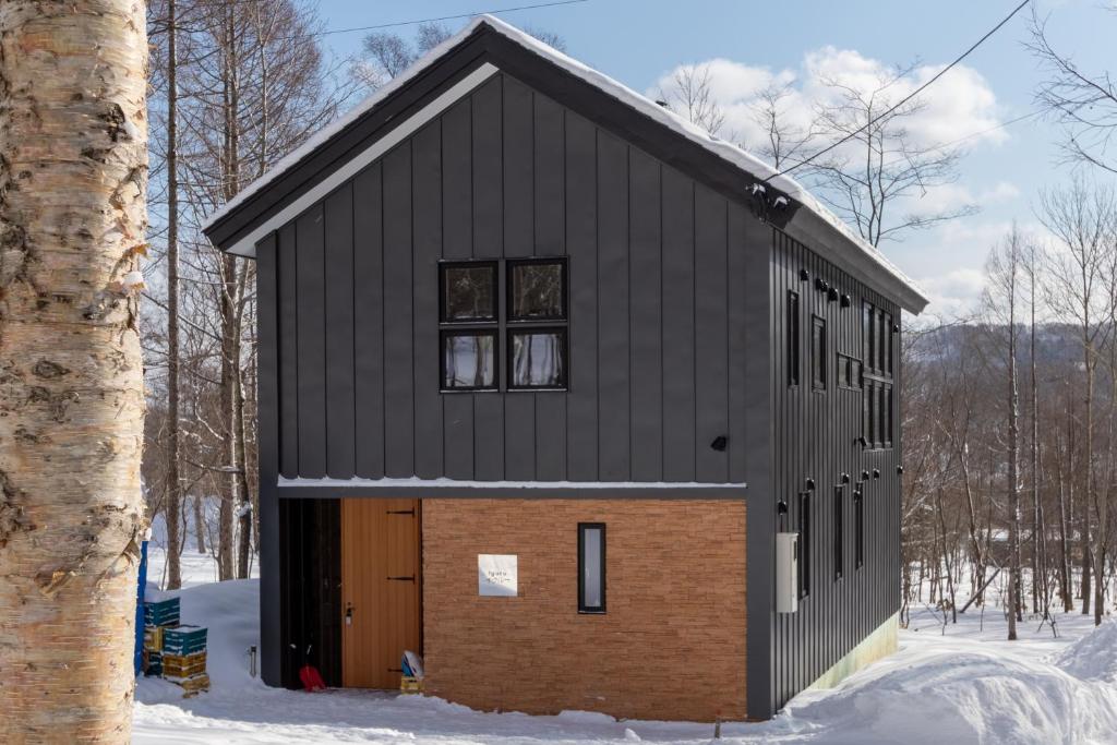 留寿都村Iguru Ski Chalet - walking distance to Rusutsu Resort的雪中带棕色门的黑色房子