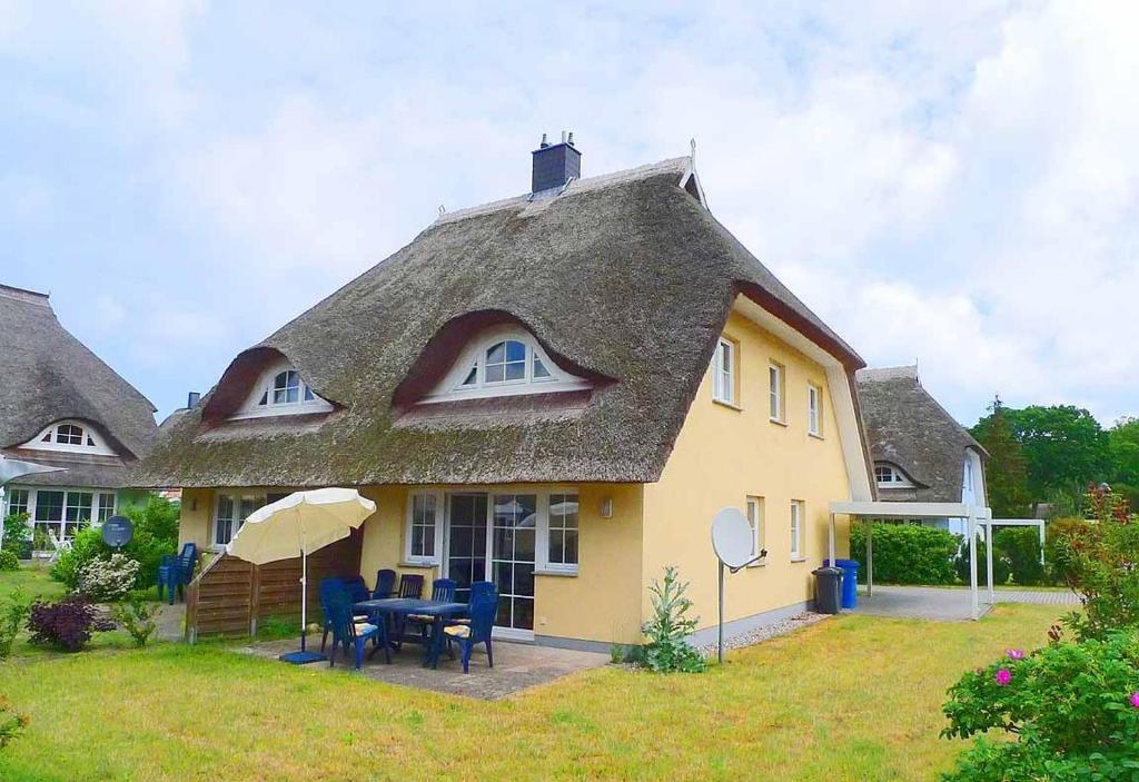 博恩Ferienhaus An der alten Waldschänke WS-11a的黄色房子,带茅草屋顶,配有桌子